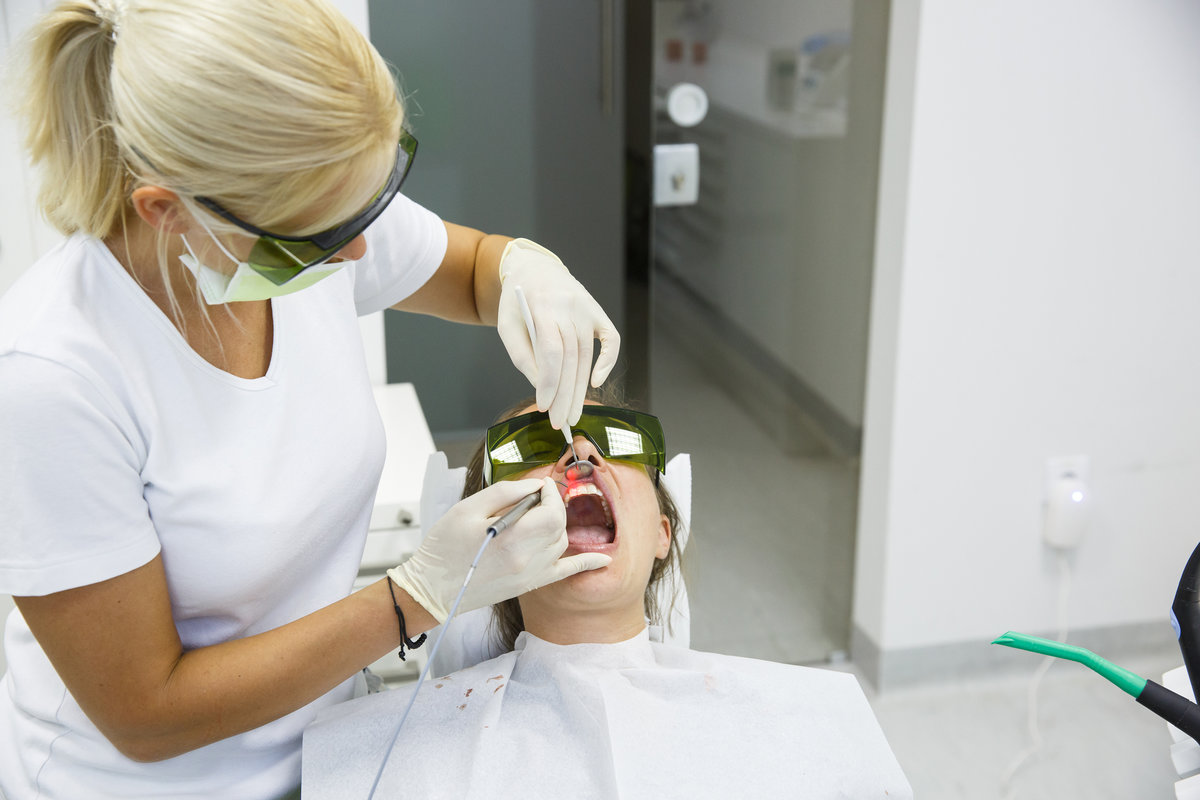 Dentist using a modern diode dental laser for periodontal care. Both wearing protective glasses, preventing eyesight damage. Periodontitis, dental hygiene, preventive procedures concept.